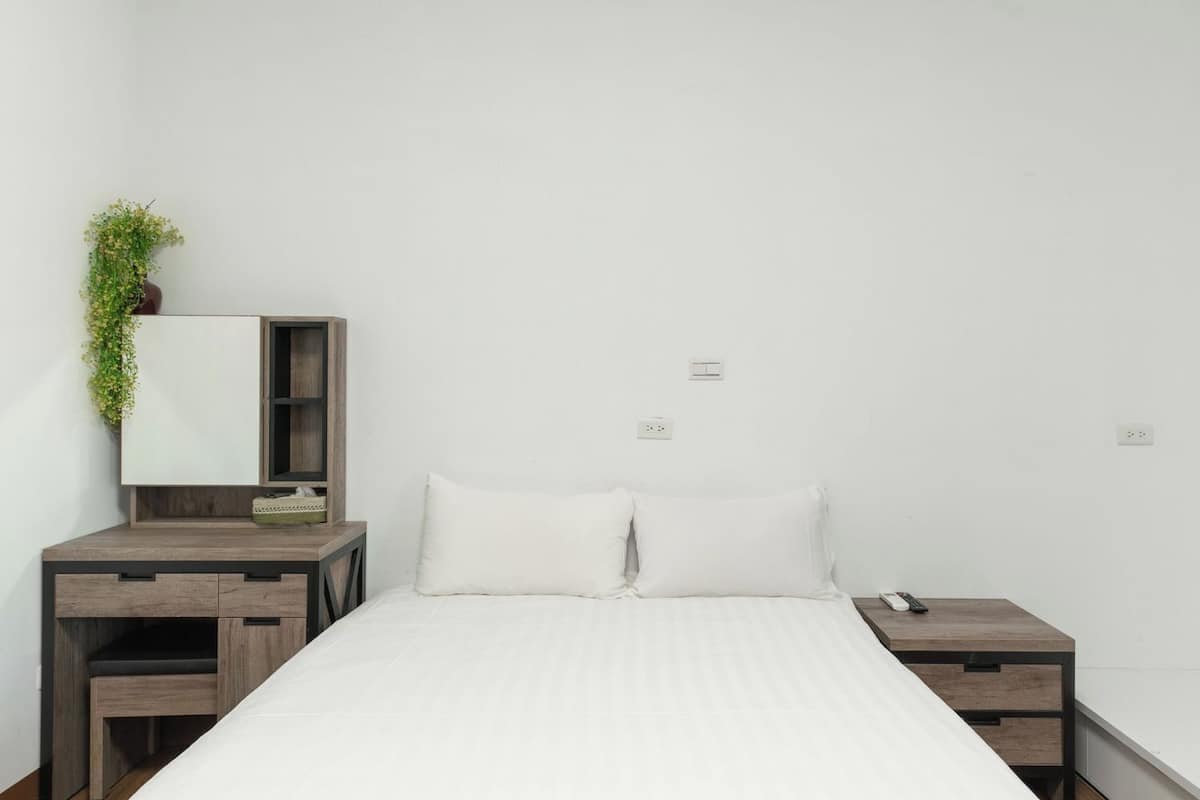 Un dormitorio minimalista con cama, mesitas de noche, un escritorio y un espejo.