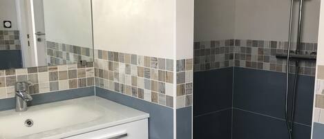 A bathroom with a white sink, a mirror, and a shower area with tiled walls.