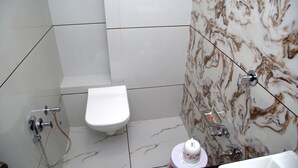 Une salle de bain avec des toilettes blanches, une douche et un mur décoré d’un motif imitant le marbre.