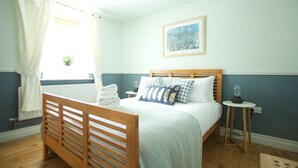 Un dormitorio con cama de madera, una mesita de noche con lámpara, un radiador y una ventana con cortinas.