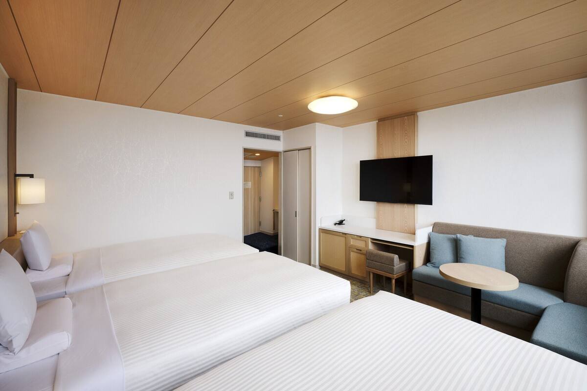 A hotel room with two beds, a desk, a television, and a seating area.