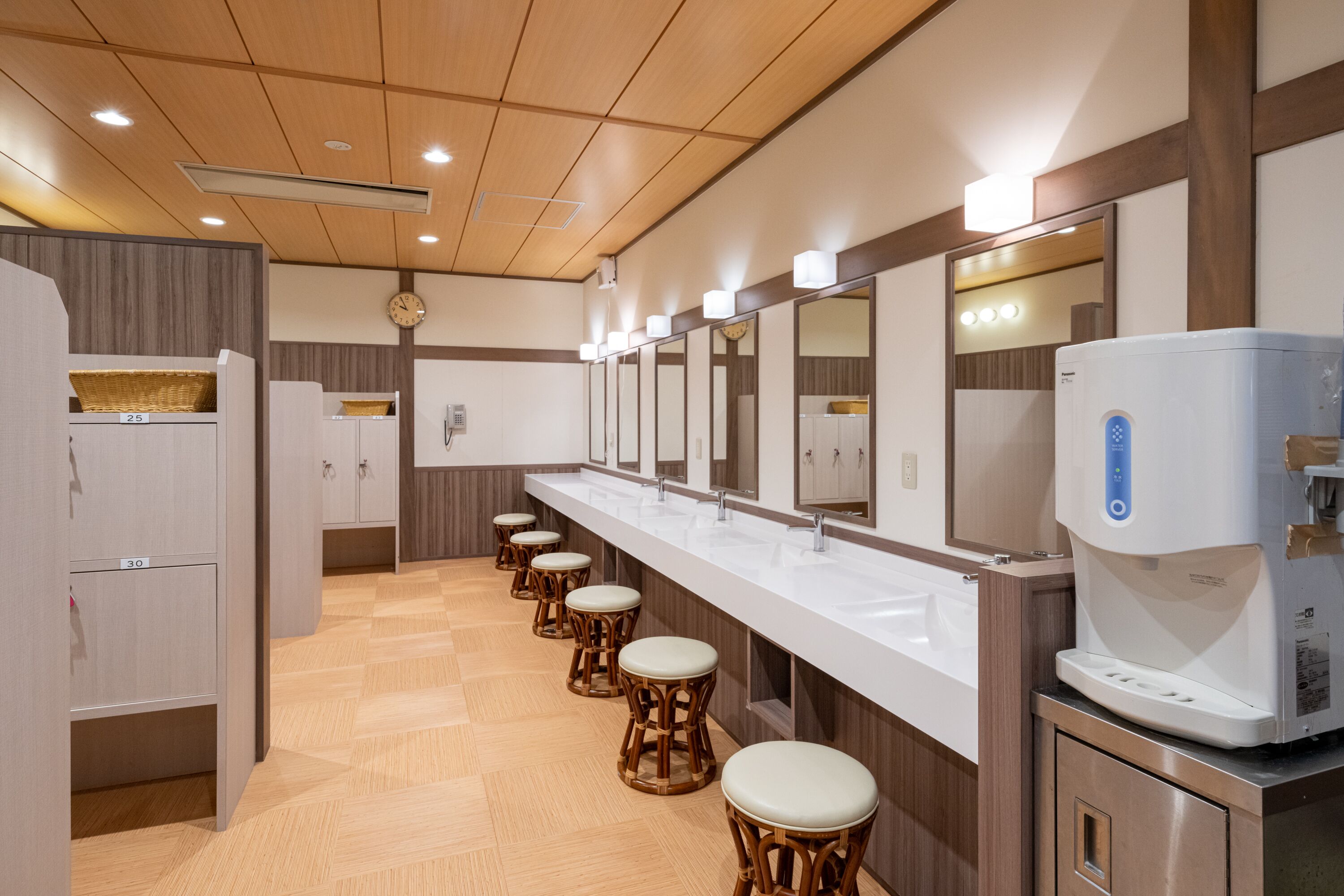 Een moderne toiletruimte met meerdere wastafels, houten krukken en een waterdispenser.