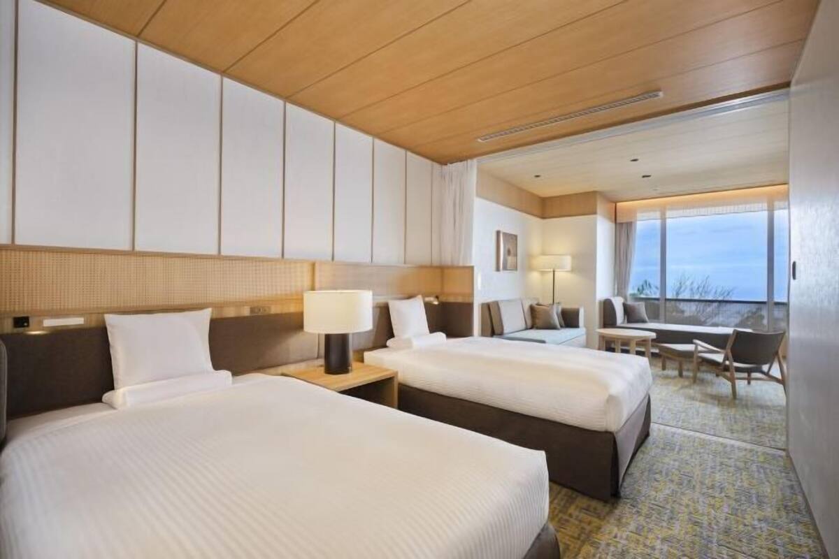 Habitación de hotel con dos camas, un escritorio, una silla y vistas al exterior.