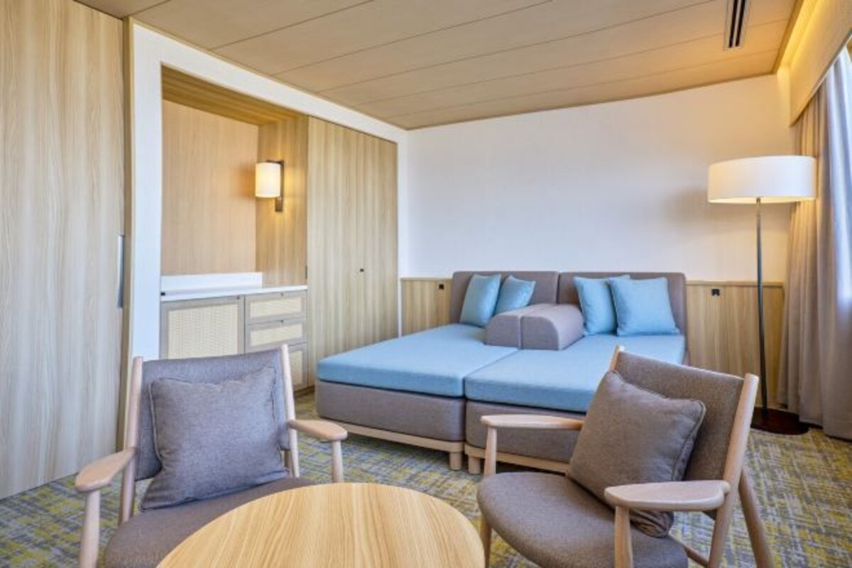 A hotel room with a bed, two armchairs, a small table, a desk, and a lamp.
