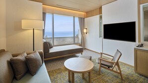Habitación de hotel con cama, sofá, televisión, lámpara y vista al mar.