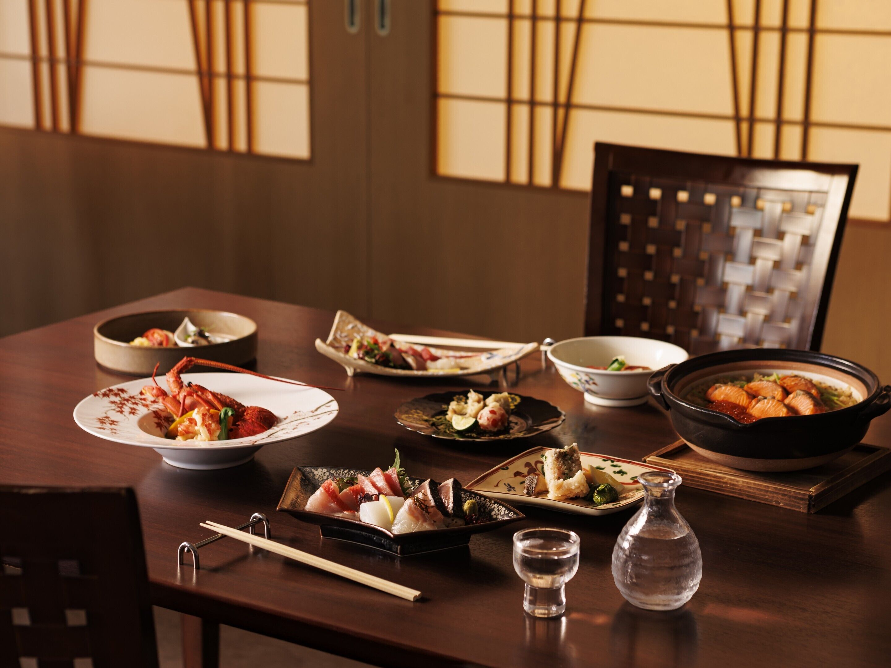 A dining table with various dishes, chopsticks, and a small glass pitcher.