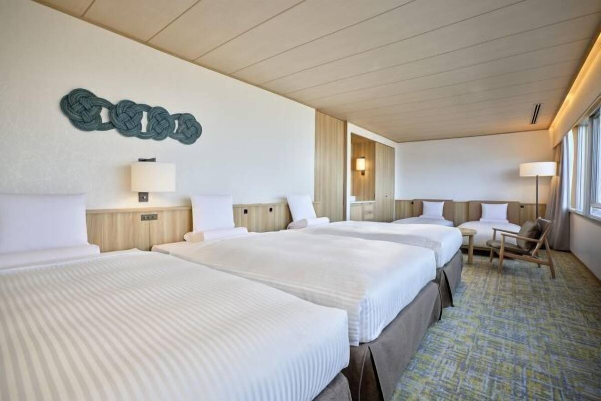 Habitación de hotel con tres camas, un escritorio, una silla y una obra de arte colgada en la pared.
