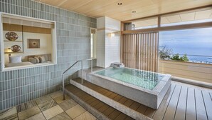Un baño moderno con un jacuzzi con cerramiento de vidrio, una zona de estar con cojines y vistas al mar.