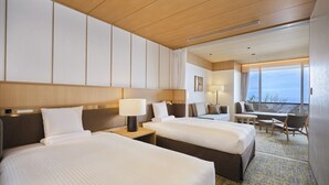 Habitación de hotel con dos camas, un sofá, un escritorio y un ventanal con vistas.