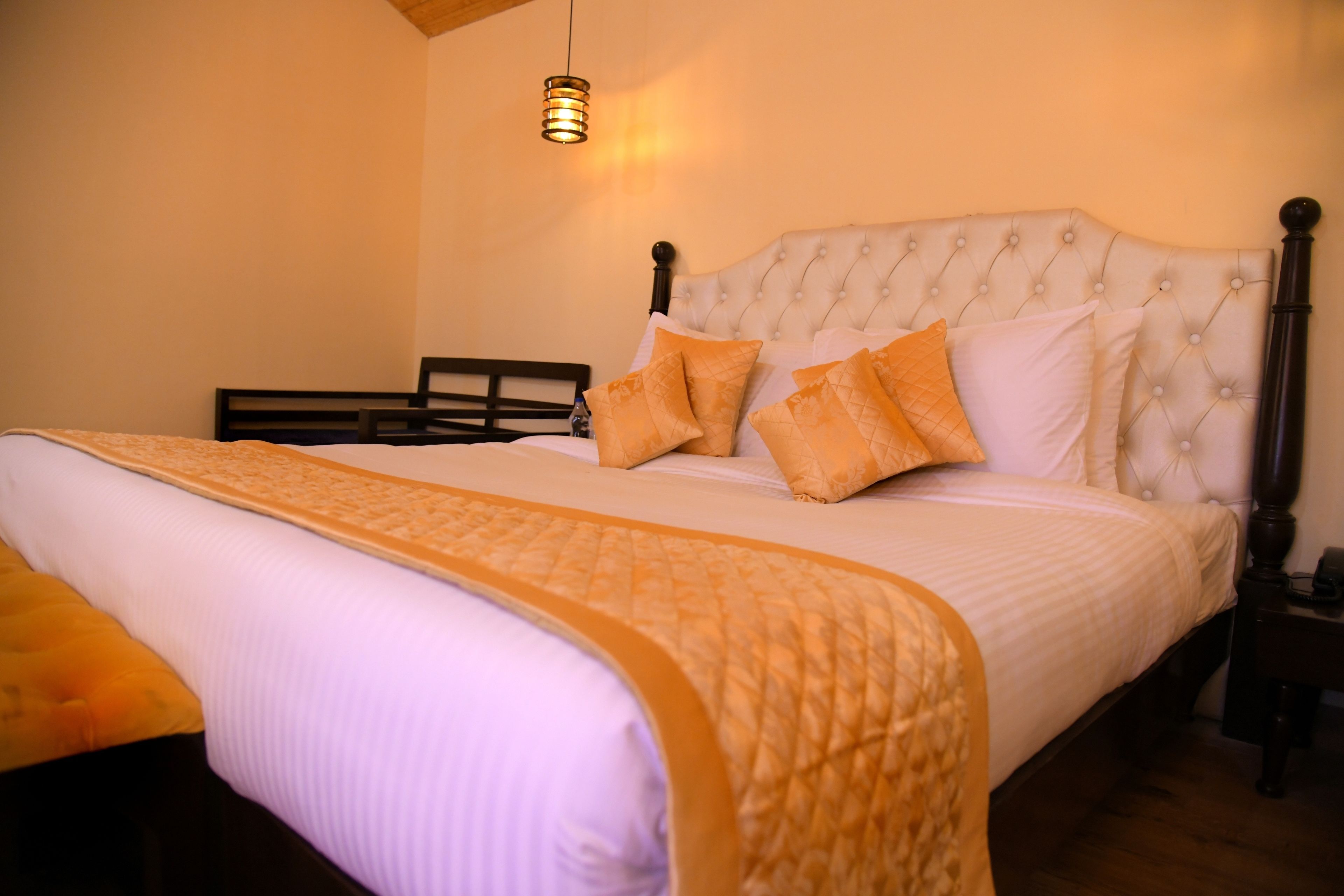 A neatly made bed with a quilted bedspread and pillows, a wooden headboard, and a hanging light fixture.