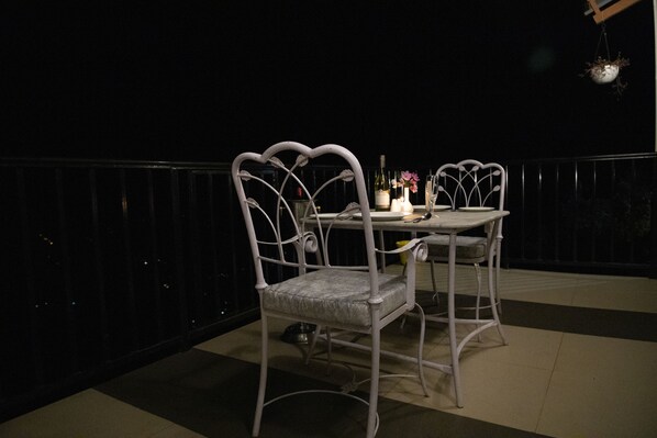 A balcony with a white metal table and chairs, a small potted plant, and a bottle of champagne.