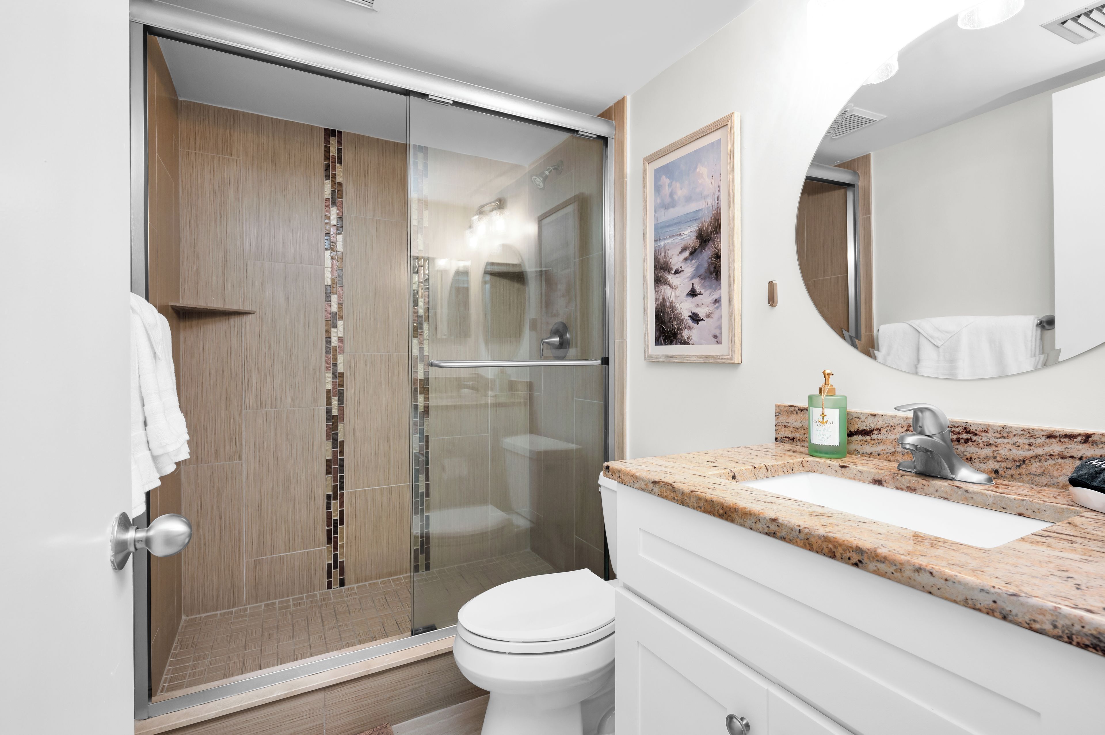 Un bagno moderno con doccia vetrata, un water bianco, un piano di lavoro in granito e un quadro incorniciato con un paesaggio.