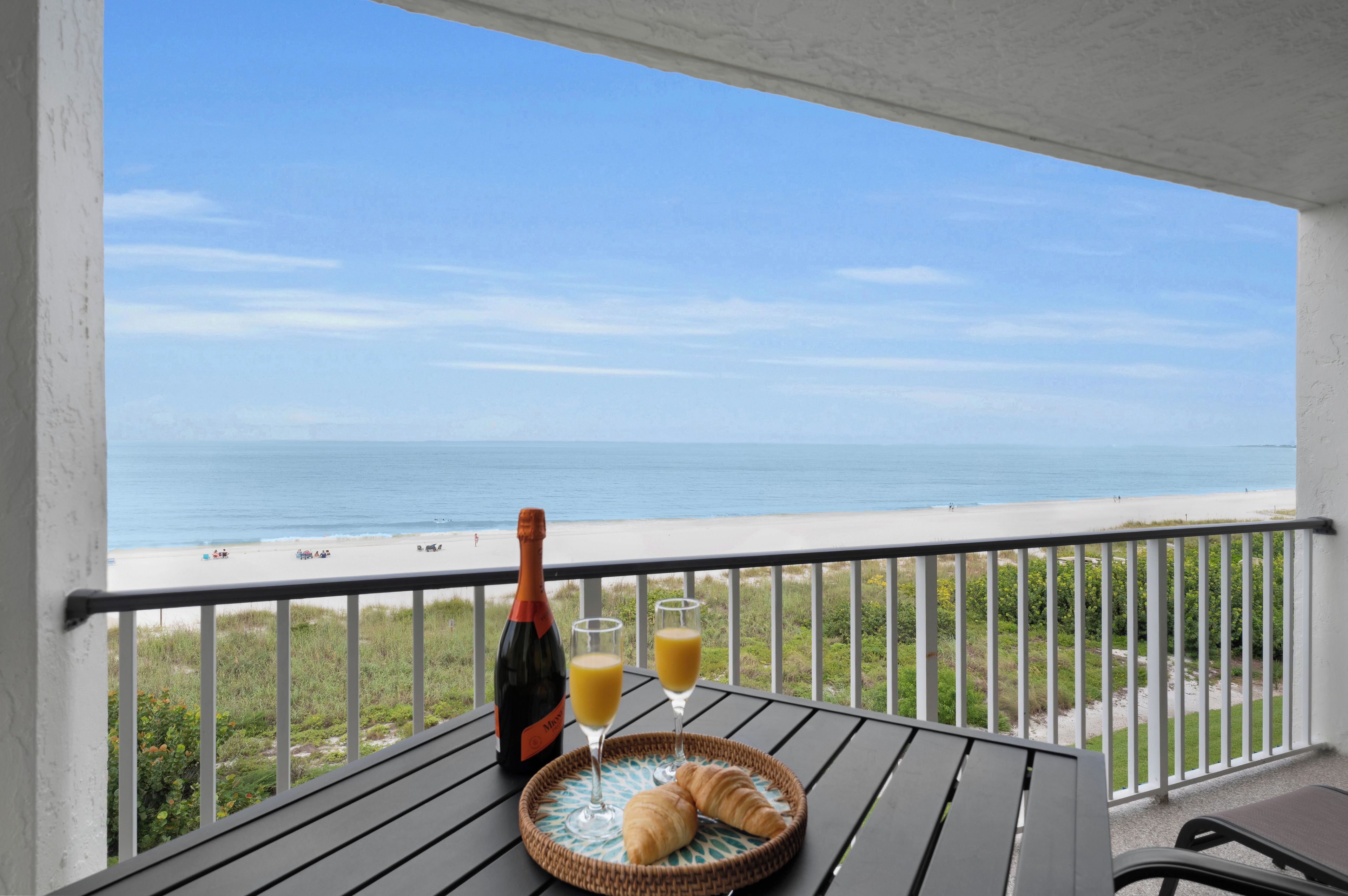 A balcony with a table set for a meal, overlooking a beach.