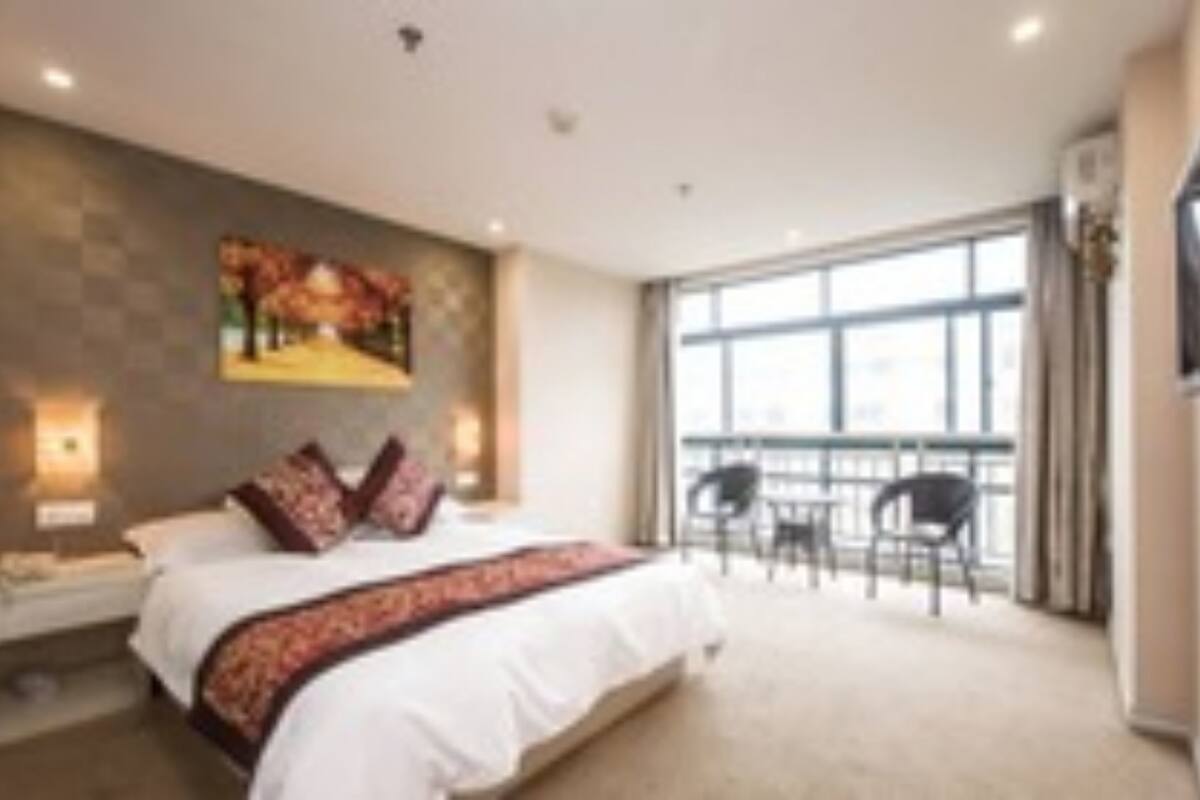 Habitación de hotel con una cama grande, un cuadro en la pared, un balcón con sillas y un ventanal amplio.