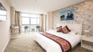 A hotel room with a large bed, a stone wall, a painting of a ship, and a view of the sea through the window. - Gang Wan Yin Xiang Hotel (Jiaxing)