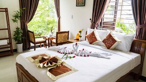 A neatly made bed with white linens and decorative pillows, a wooden chair, a small table with a vase of flowers, and a potted plant. - Golden Soulmate Homestay (Da Nang)