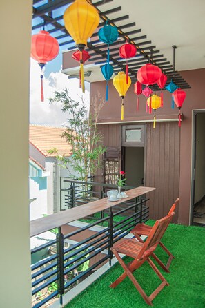A balcony with a wooden table and chairs, a bamboo plant, and colorful lanterns hanging above. - Golden Soulmate Homestay (Da Nang)