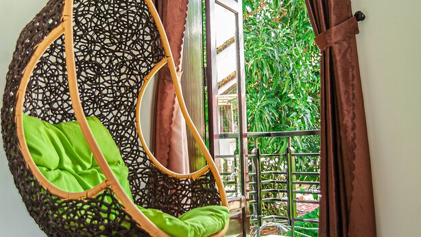 A hanging chair with a green cushion in a room with a view of a garden through a window with brown curtains. - Golden Soulmate Homestay (Da Nang)