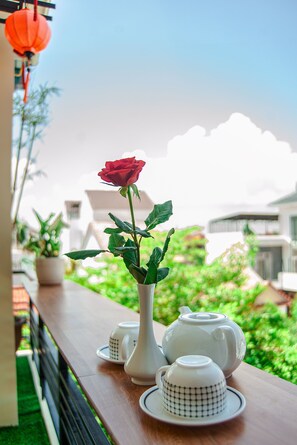 A wooden table with a white teapot, a teacup, and a rose in a vase. - Golden Soulmate Homestay (Da Nang)
