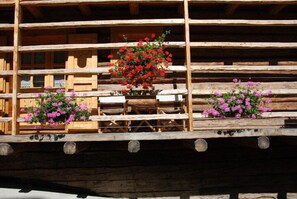 A wooden structure with multiple levels, each with a wooden railing and flower planters. - Hotel Garni Plueme (Sauris)
