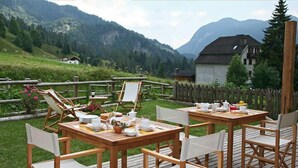 An outdoor dining area with wooden tables and chairs, set against a backdrop of mountains and a wooden fence. - Hotel Garni Plueme (Sauris)
