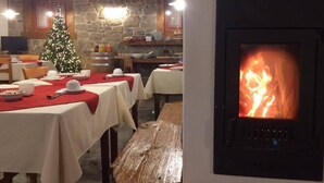 A dining area with tables set for a meal, a stone wall, a Christmas tree, and a wood-burning stove. - Hotel Garni Plueme (Sauris)