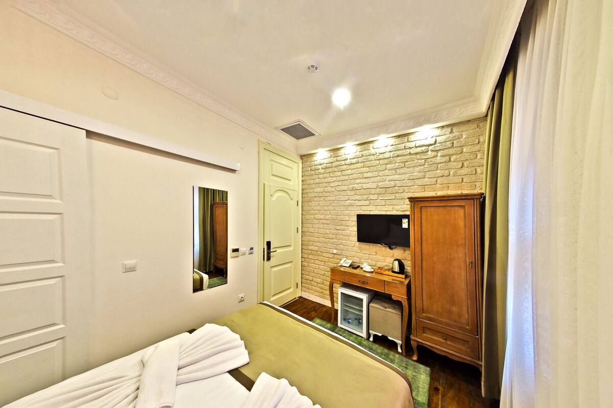 A hotel room with a bed, a desk with a television, a wardrobe, and a mirror on the wall.