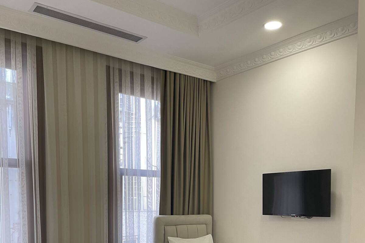 A hotel room with two beds, a flat-screen TV mounted on the wall, and a large window with curtains.