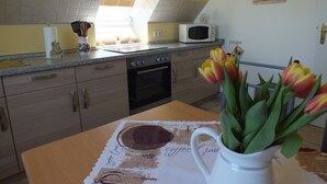 Une cuisine équipée d’un four à micro-ondes, d’un four traditionnel et d’une fenêtre avec des stores. On y trouve une table avec un set de table sur le thème du café et un vase de tulipes.