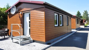 A modern, single-story wooden building with a satellite dish, a small outdoor seating area, and a metal staircase leading to the entrance. - Campingplatz Am Waldbad (Schleusingen)