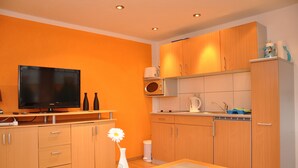 A compact kitchen with wooden cabinets, a microwave, and a television. - Campingplatz Am Waldbad (Schleusingen)