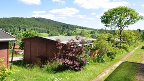A rural setting with a wooden shed, a tree, and a path leading to a house. - Campingplatz Am Waldbad (Schleusingen)