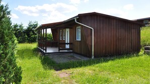A wooden cabin with a porch, a door, and a window. - Campingplatz Am Waldbad (Schleusingen)