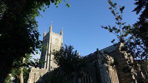 A historic stone building with a prominent tower and arched windows, surrounded by trees. - Saffron House (Fowey)