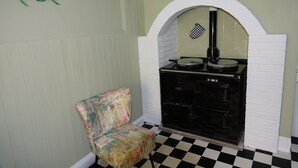 A room with a checkered floor, a patterned armchair, a black stove, and a wall clock. - Saffron House (Fowey)