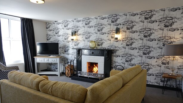 A living room with a sofa, a fireplace, a television, and a patterned wallpaper. - Saffron House (Fowey)