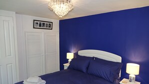 A bedroom with a large bed, two bedside tables with lamps, a chandelier, and a framed picture on the wall. - Saffron House (Fowey)