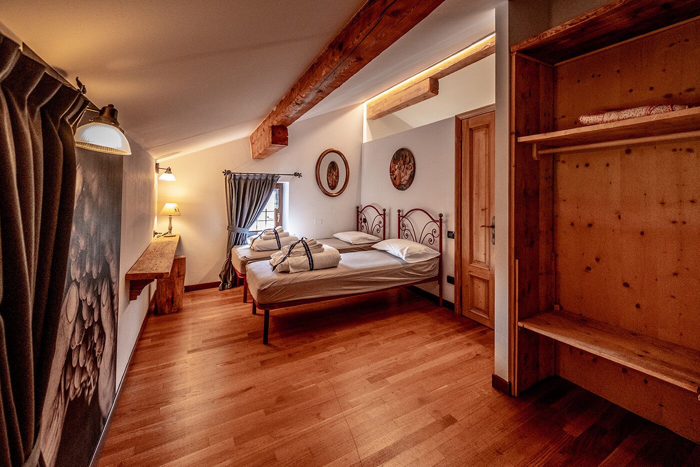 A cozy bedroom with a wooden floor, a bed with white linens, a wooden bench, and a desk with a lamp.