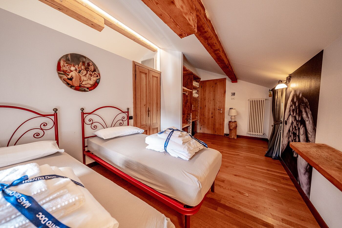A hotel room with two beds, wooden beams, a radiator, and a painting on the wall.
