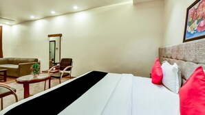 Habitación de hotel con cama, sofá, sillón, una mesita y un cuadro en la pared.
