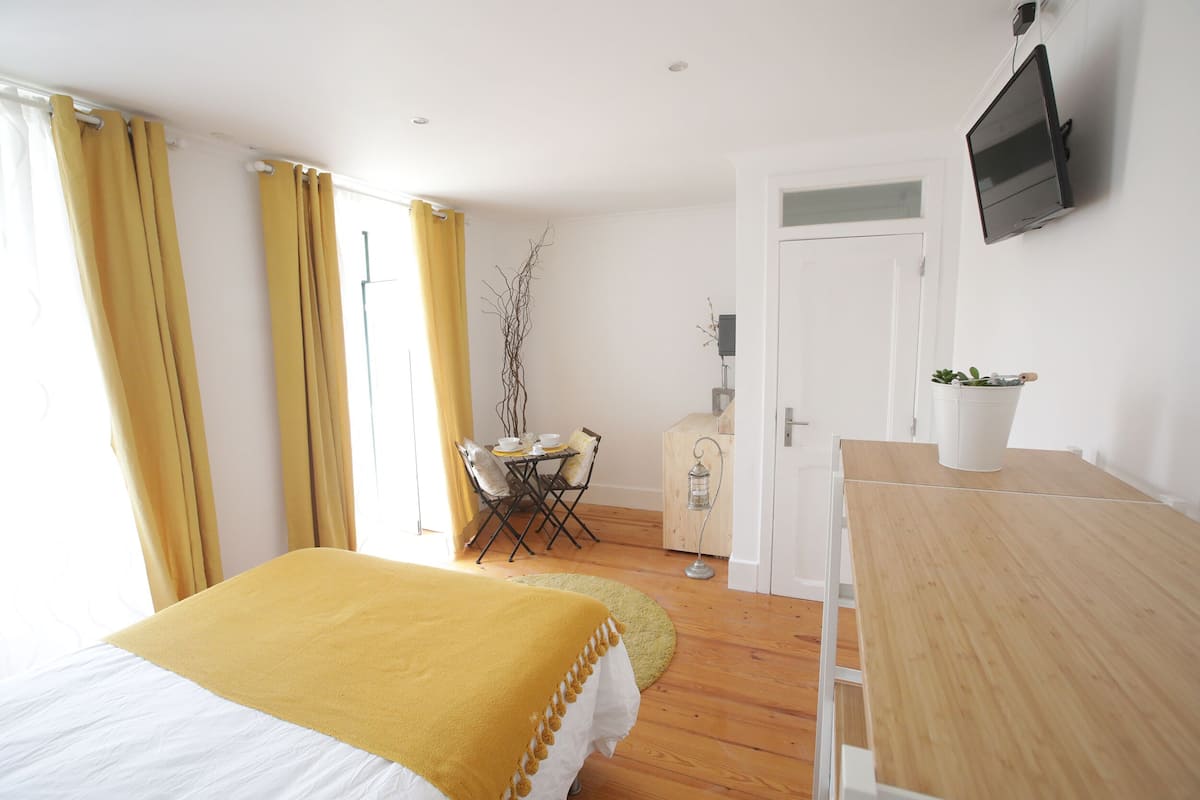 A bedroom with a bed, a wooden desk, a television, and a small table with a plant.