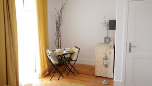 A dining area with a table set for two, a chair, a small cabinet, and a decorative branch.