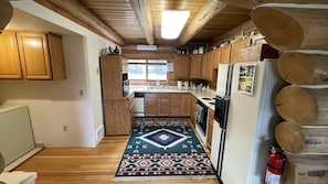 A compact kitchen with wooden cabinets, a refrigerator, a stove, and a window providing natural light.
