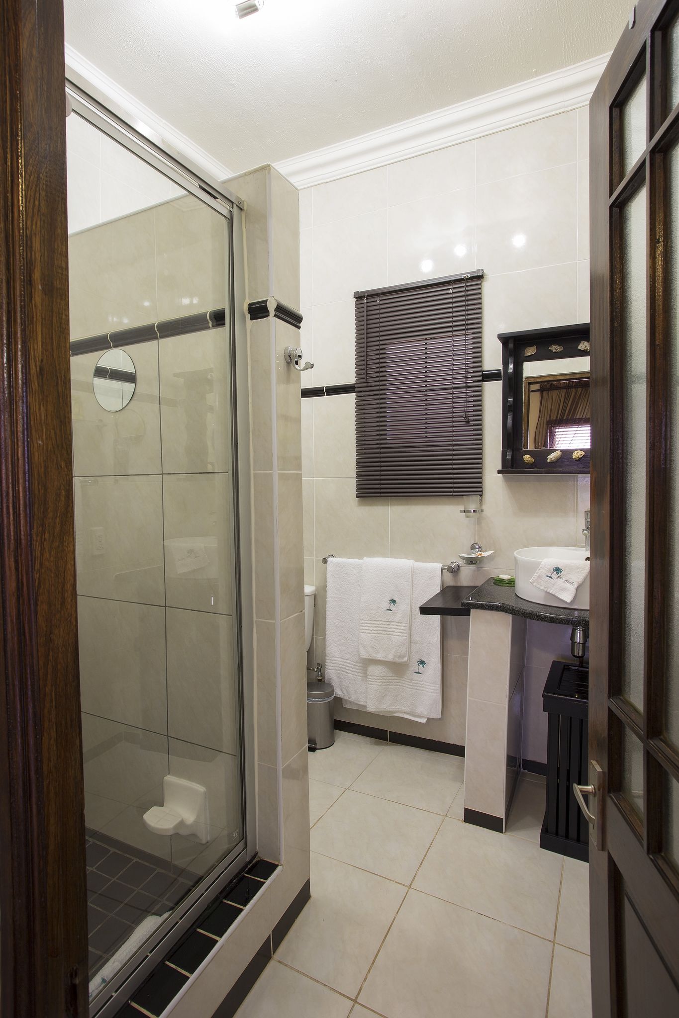 Une salle de bain avec une douche à parois de verre, un lavabo avec un miroir au-dessus et une fenêtre avec des stores.