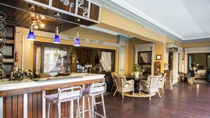 Un espace bar doté d’un comptoir en bois, de tabourets de bar, de chaises en osier et de lampes suspendues bleues.