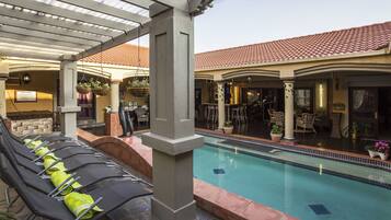 A pool area with lounge chairs, a covered seating area, and a bar.