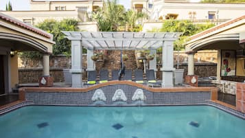 Una piscina al aire libre, sombrillas, sillones reclinables de piscina