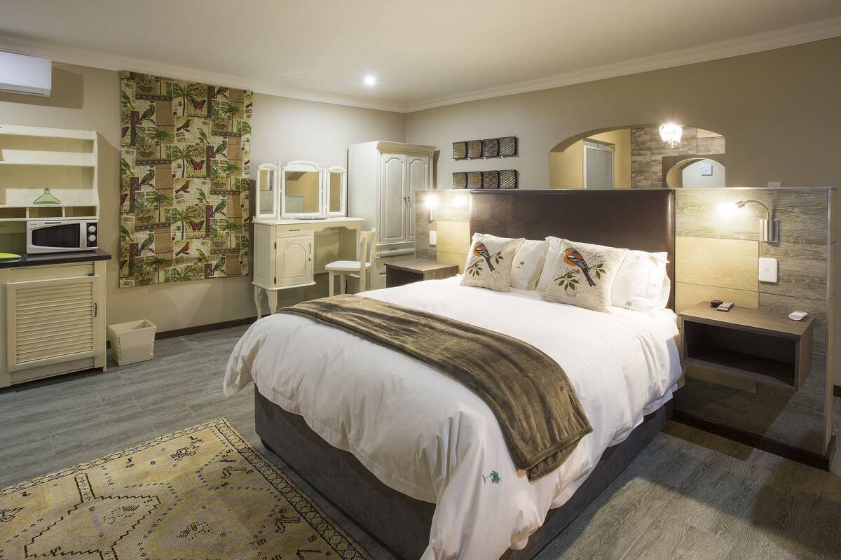 A bedroom with a large bed, bedside tables, a wardrobe, a desk with a chair, a microwave, and a patterned wall.