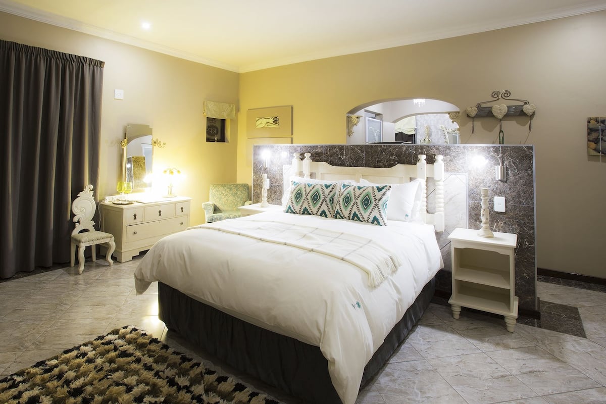 A bedroom with a large bed, bedside tables, a nightstand, a mirror, and a wall-mounted shelf.