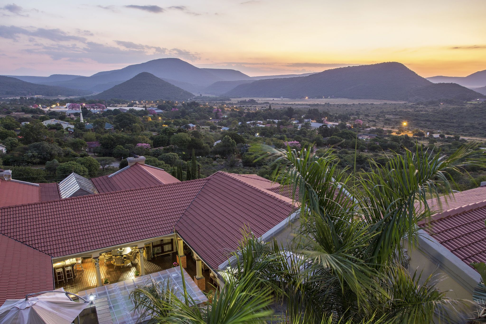 A residential area with houses featuring red roofs, surrounded by greenery and hills in the background.